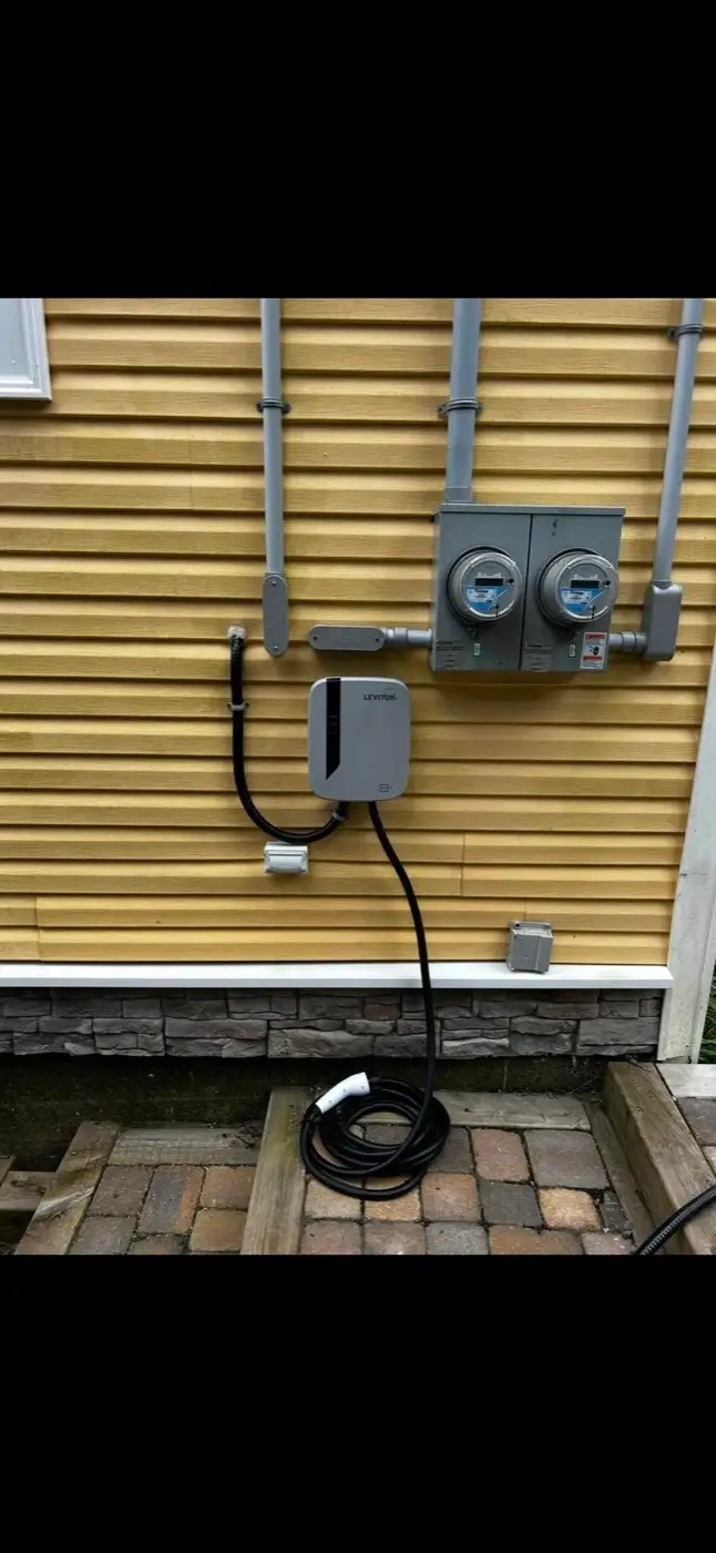 Wall mounted Level 2 EV charger installed beside two meter bases, cord coiled below